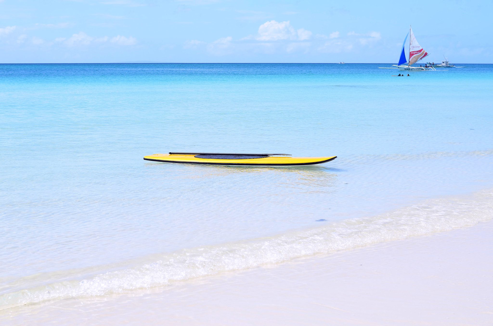 Yellow paddle board in the water of White Beach Boracay Island with a local paraw boat in the background. Article Boracay Ranked 10th Among Worlds Best islands, by MY RANGGO Philippine Hospitality Magazine