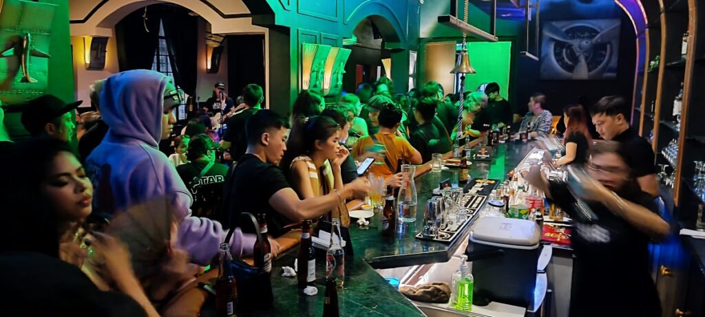 A photo of Opening Night at Hangar 18 Ermita.  The photo shows a long bar with customers sitting and drinking