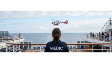 Photo of a medic in a blue uniform on the deck of a cruise ship, looking at a medic helicopter getting ready to land for a medical emergency on a cruise ship