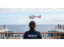 Photo of a medic in a blue uniform on the deck of a cruise ship, looking at a medic helicopter getting ready to land for a medical emergency on a cruise ship